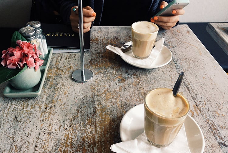 Person on phone with two cups of coffee on table